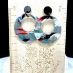 Lightweight drop hoop earrings in a marbled mix of turquoise, red, black, white, and metallic tones, finished with glossy black stud tops.